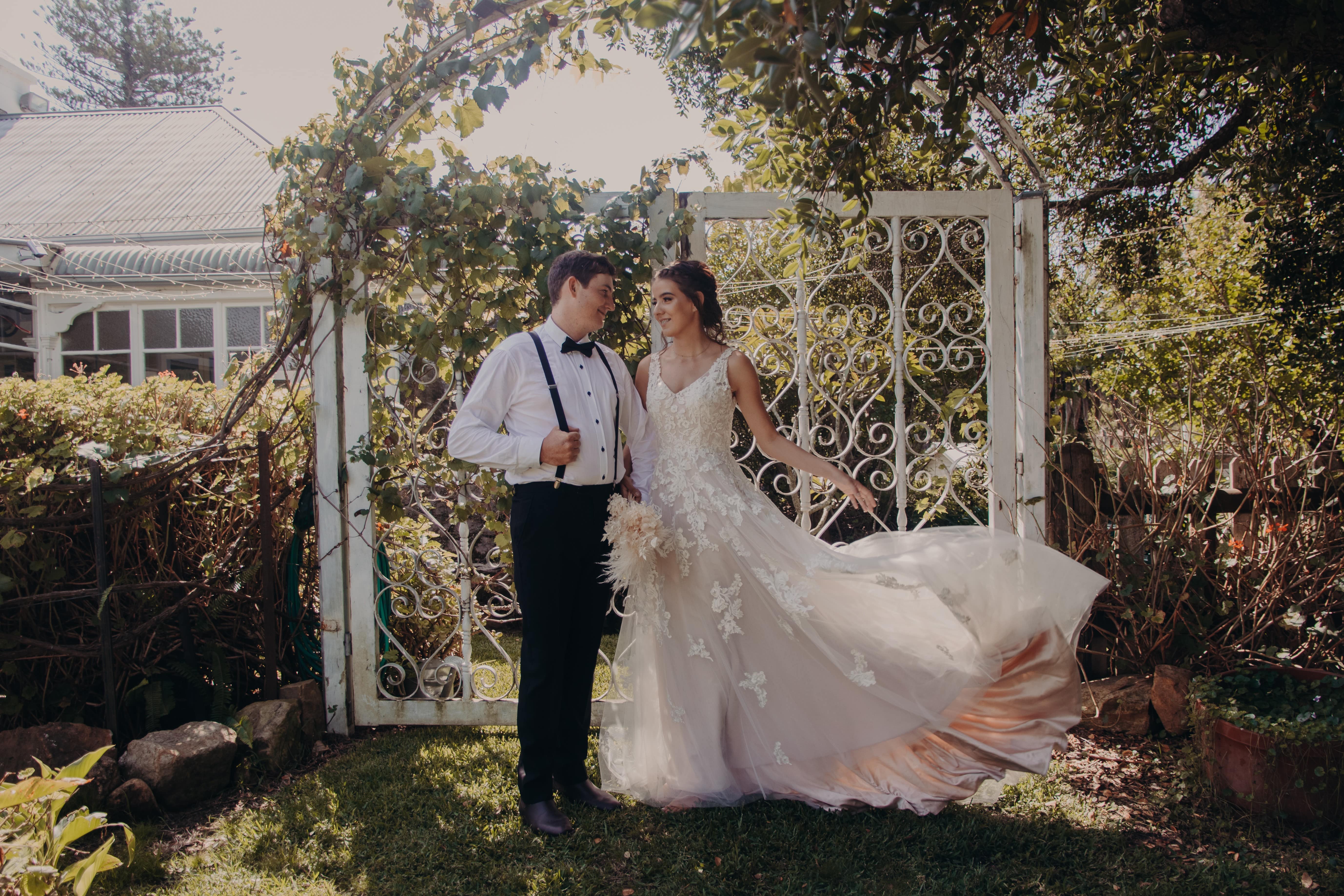 Wedding couple with large iron gatecovered in grape vines with Tanilba House behind