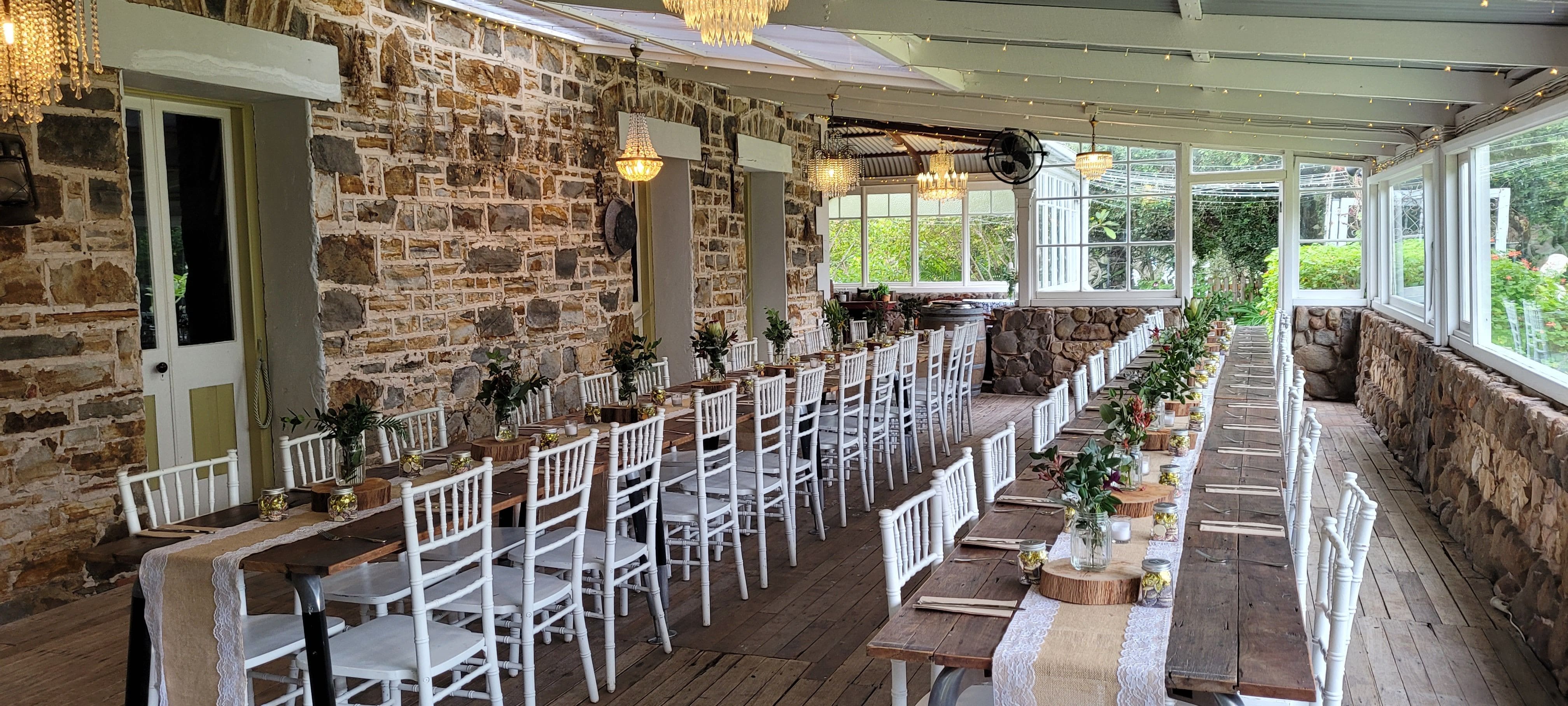 Large stone walled conservatory lit by various chandeliers with two long banqueting tables styled with rustic tables and rustic decorations