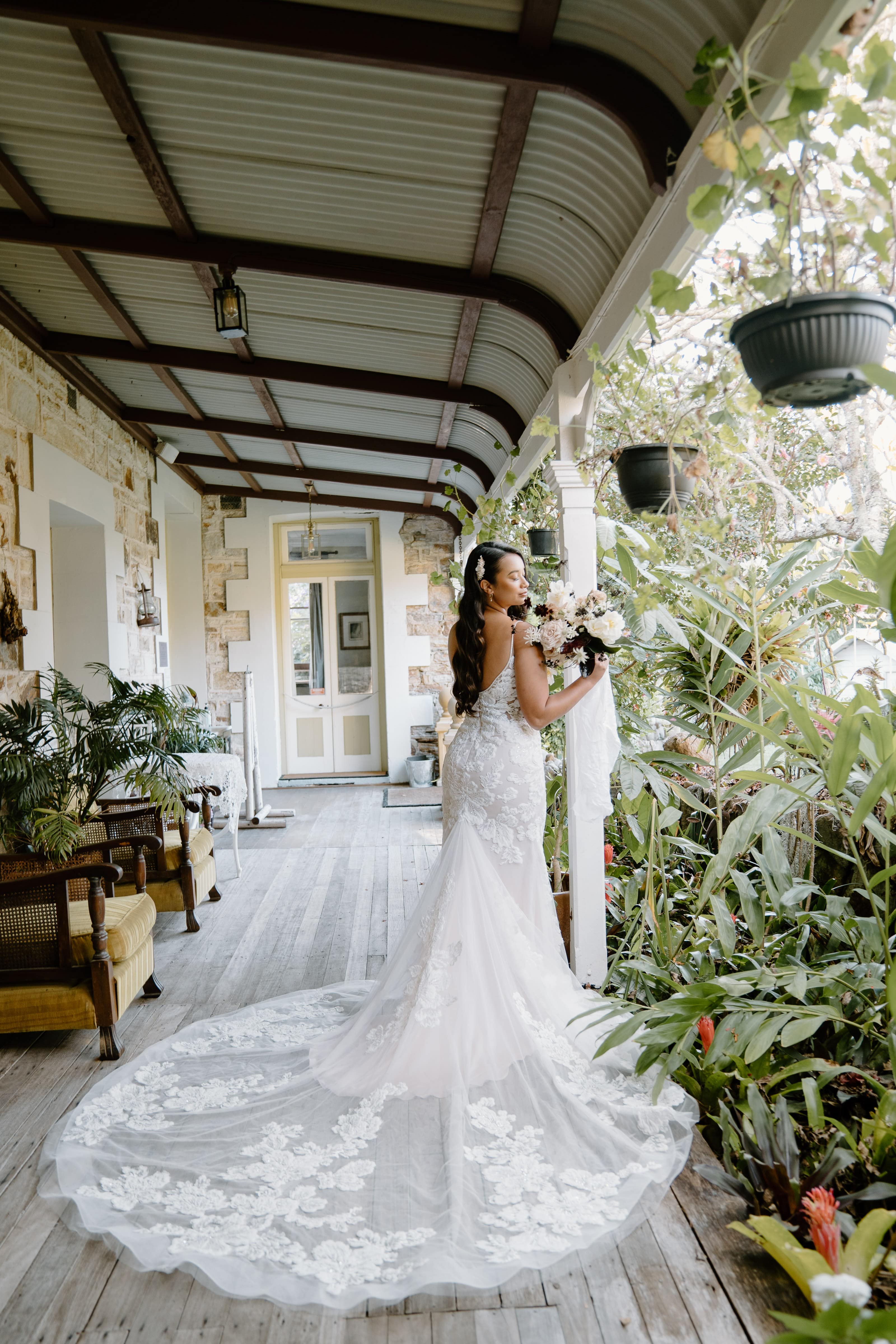 Wide colonial verandahs with garden, vintage chairs and bride with long train looking down verandah