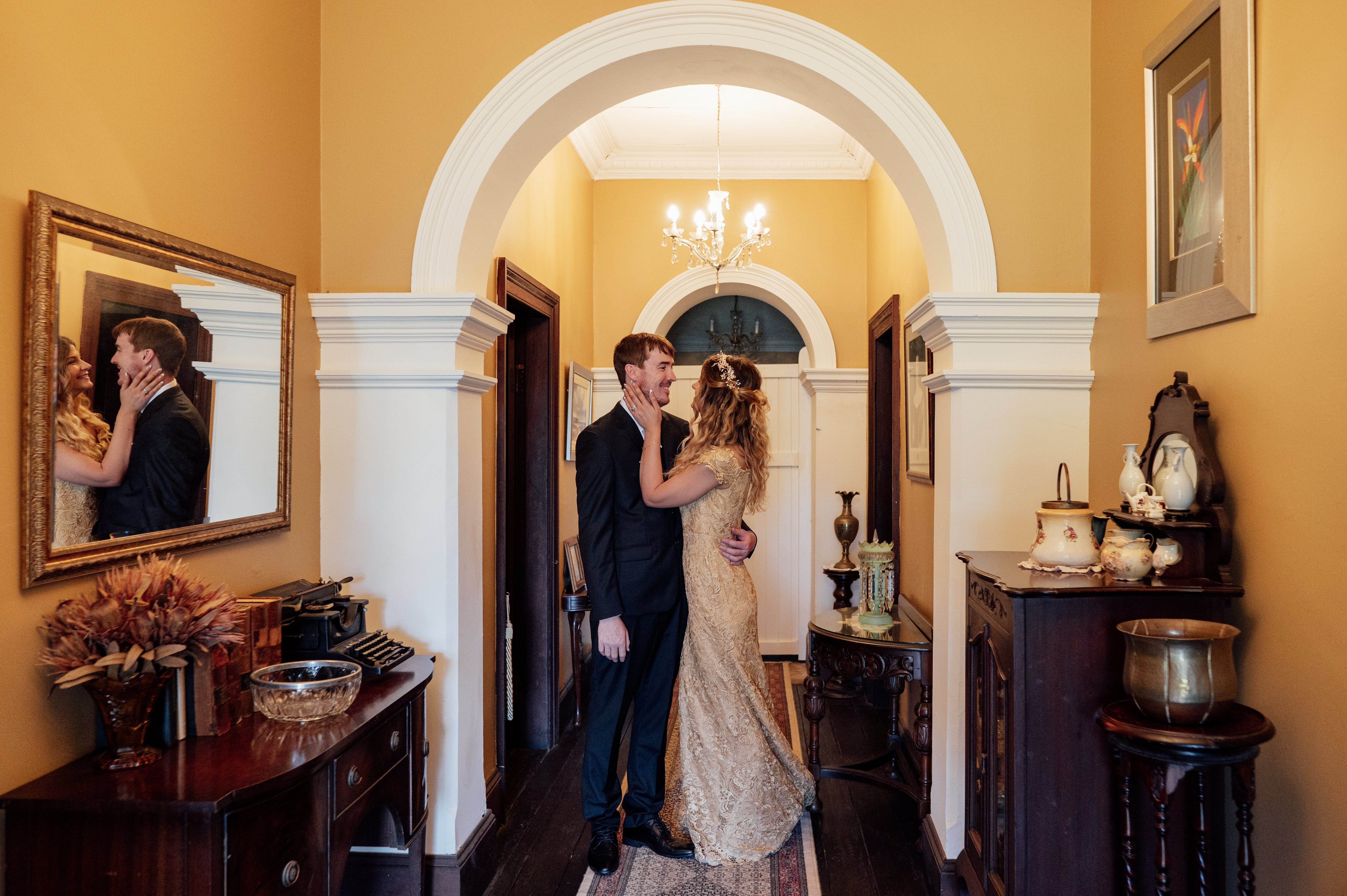 Wedding couple in colonial hall framed by various antiques, chandeliers and mirror