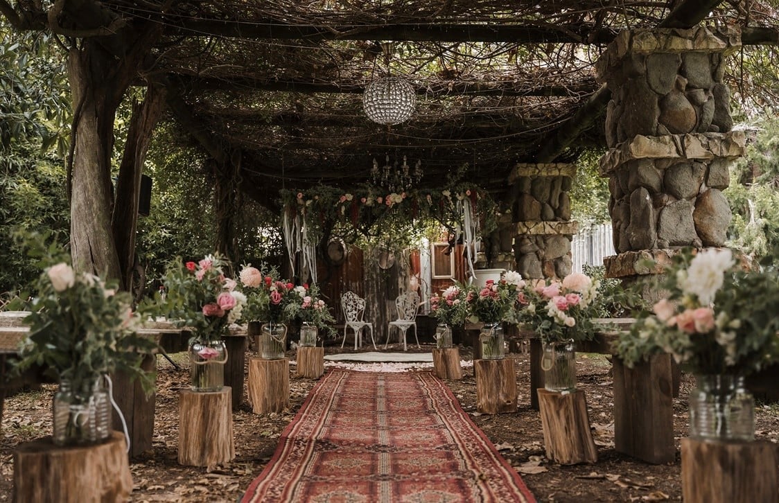 20 meter long wedding arbour covered in 7 different vines with rugs and rustic benches plus wooden stumps decorated with wedding flowers
