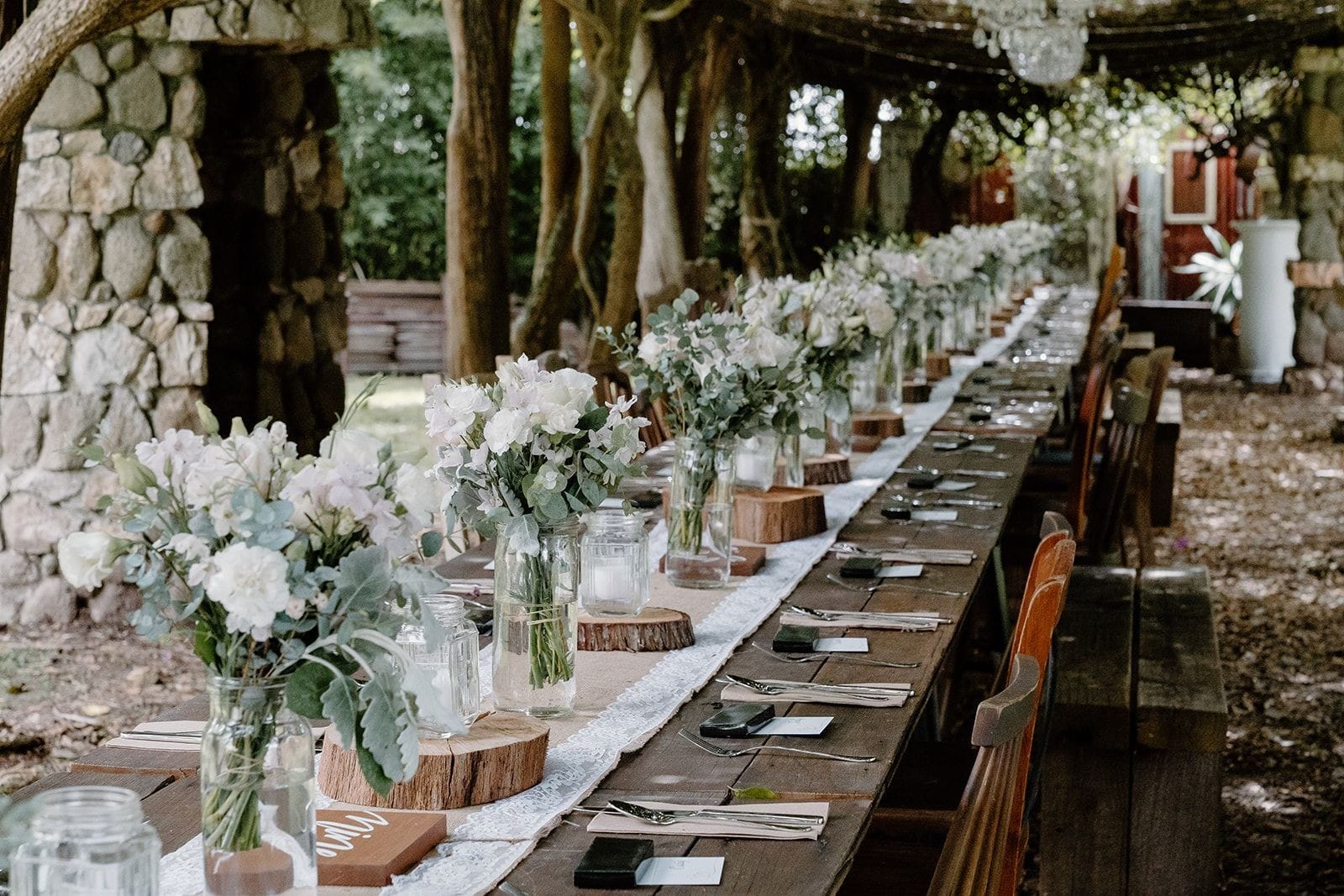Rustic 20m long garden arbour with long rustic tables and vintage styling with white florals under vintage chandeliers