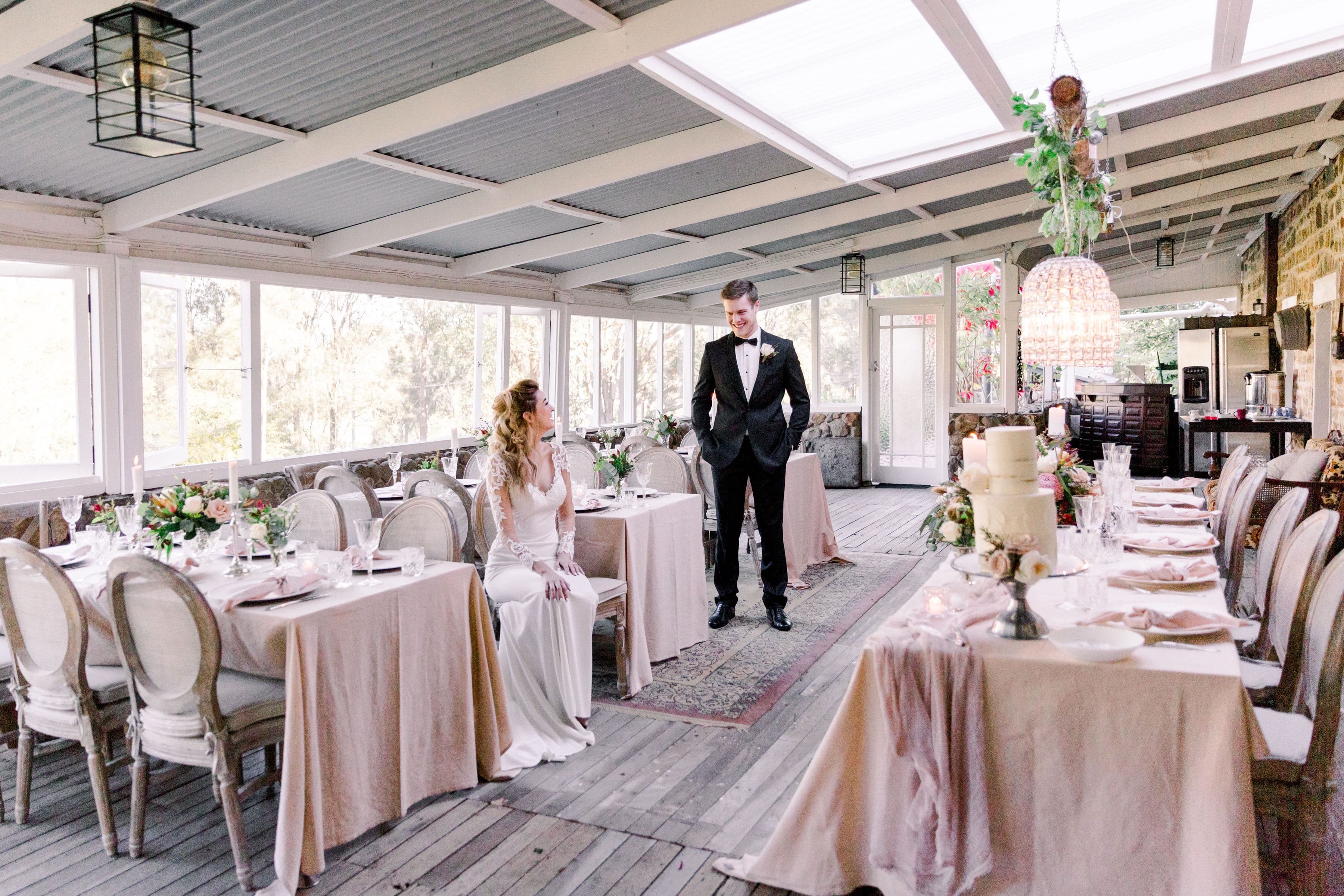Historic large stone and wood conservatory styled with soft pastel pinks and chandeliers with bride and groom